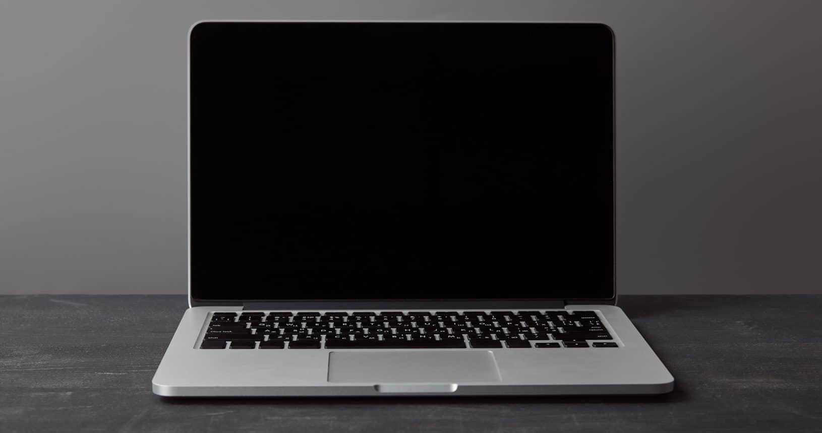 Laptop mit leerem Bildschirm auf einer dunklen, strukturierten Oberfläche in Grau