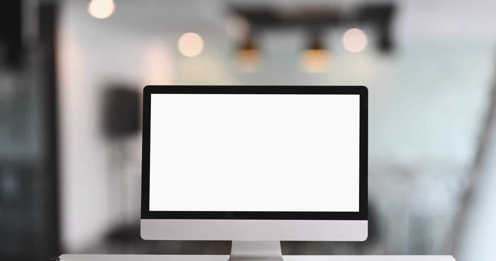 Computerbildschirm am Arbeitsplatz mit weißem, leerem Bildschirm auf einem weißen Tisch.